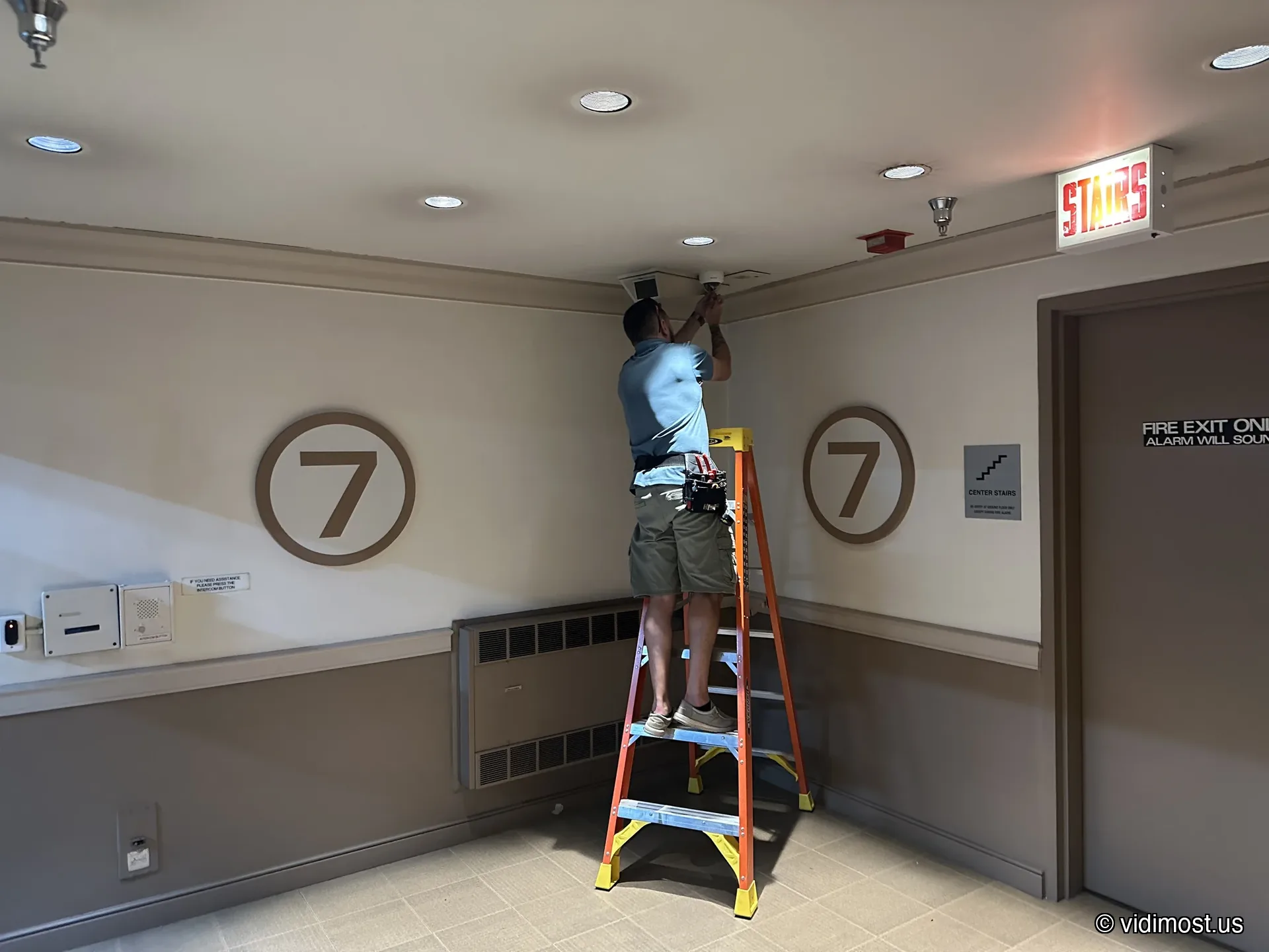 Technician servicing a security camera in a Chicago condo building hallway near the elevator lobby